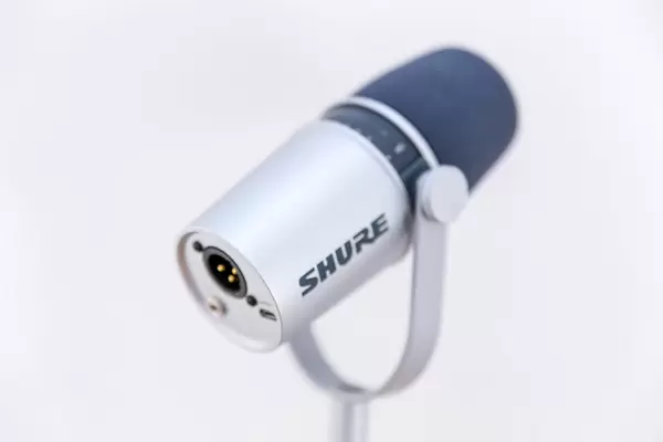 Nahaufnahme des Shure MV 7 Silver Studio-Mikrofron mit Touchpanel, Shockmount und Halterung, vor hellem Hintergrund