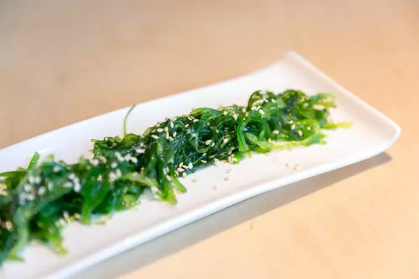 Nahaufnahme des veganen Algensalats "Goma Wakame" mit Sesamkernen bestreut, auf einem weißen länglichen Teller