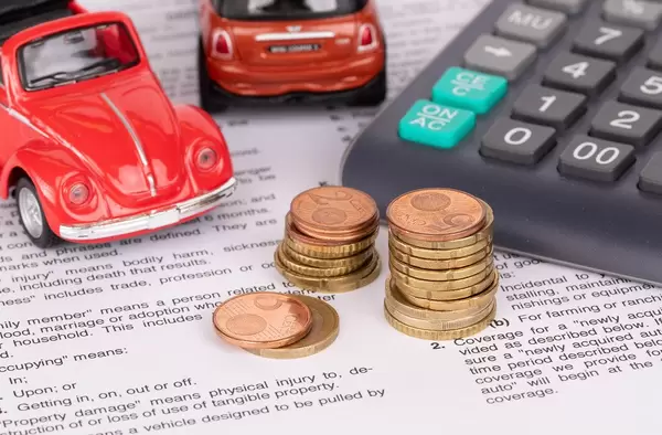 Nahaufnahme: drei Stapel Euromünzen, zwei Spielzeugautos, Taschenrechner und juristischer Text