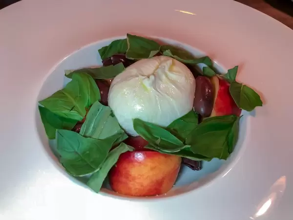 Nahaufnahme einer Burrata mit marinierten Tomaten, Pfirsich, Kalamata Oliven und Basilikum