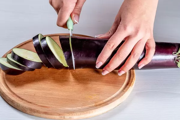 Nahaufnahme einer Frauenhand mit Messer, beim schneiden einer Aubergine