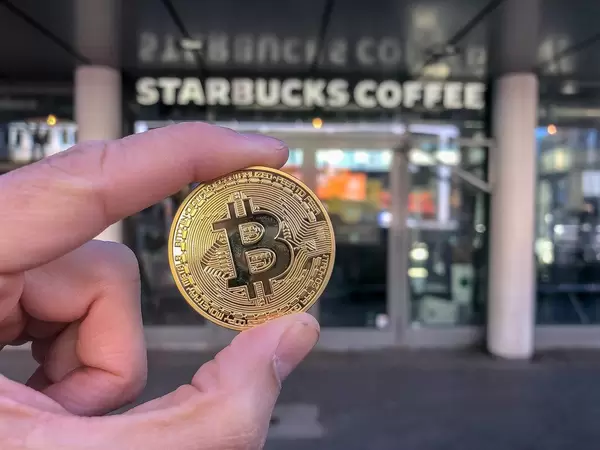 Nahaufnahme einer goldenen-Bitcoin-Münze vor Starbucks Coffee House am Friesenplatz in der Kölner Altstadt-Nord
