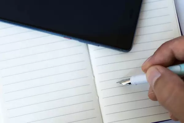 Nahaufnahme einer Hand eines Mannes der einen Schreibstift über einem Notizheft hält