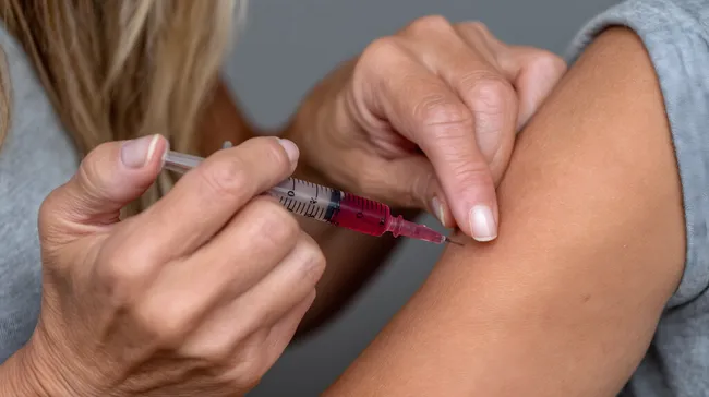 Nahaufnahme einer Impfung mit Spritze im Oberarm einer Frau