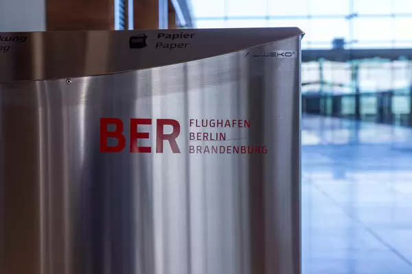 Nahaufnahme einer Mülltonne aus Metall mit BER Flughafen Berlin Brandenburg Logo in Rot
