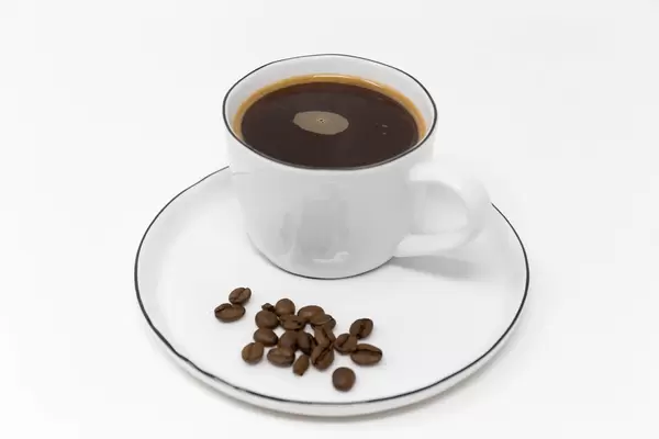 Nahaufnahme einer Tasse schwarzer Kaffee auf einem weißen Teller mit Kaffeebohnen serviert