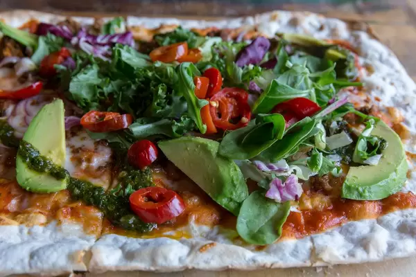 Nahaufnahme eines bunten Fladenbrots mit der veganen Fleischalternative Chili-Härkis, Avocado, Salat, roten Zwiebeln, Tomatensauce & Chimichurri.
