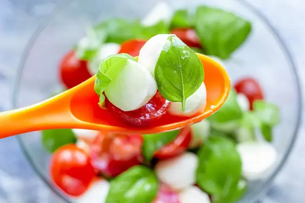 Nahaufnahme eines Capresesalats auf einem orangen Plastik-Löffel