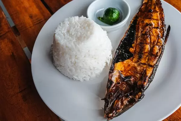 Nahaufnahme eines gegrillten Milchfisch mit Reis, auf einem Holztisch