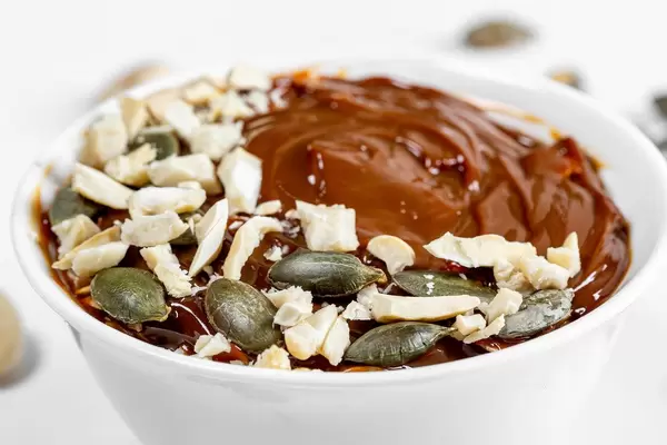 Nahaufnahme eines süßen, schokoladigen Nachttischs mit Kondensmilch, Cashewnüsse und Kürbiskernen