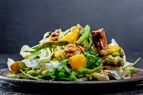 Nahaufnahme eines veganen Salats, mit Orangen, Nüssen, Brokkoli, Salatblätter und Spargel