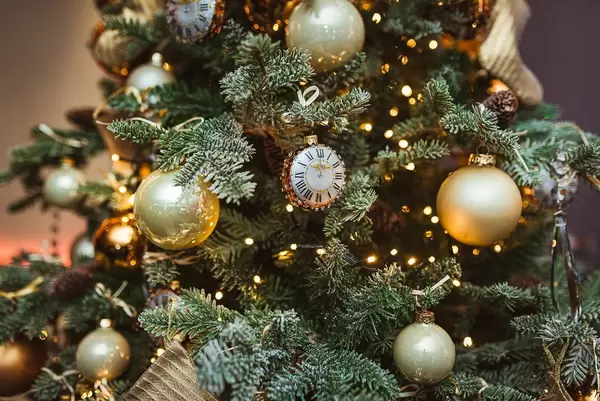 Nahaufnahme eines Weihnachtsbaumes beschmückt mit Weihnachtskugeln und einer goldenen Uhr