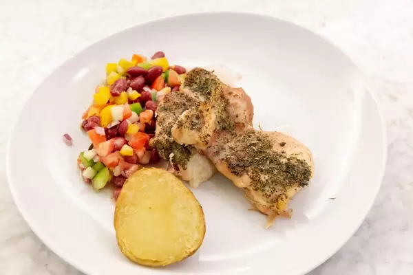 Nahaufnahme - Hähnchen in Kräutersauce mit Backkartoffel und gemischtem Salat mit Bohnen