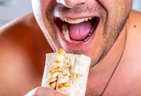 Nahaufnahme hungriger Mann mit geöffnetem Mund und frisch gebratenem Shawarma in der Hand