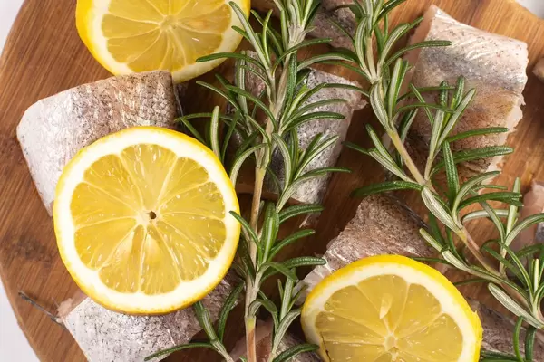 Nahaufnahme in Stücke geschnittener Hecht mit Zitronenscheiben und Rosmarin auf hölzernem Küchenbrett