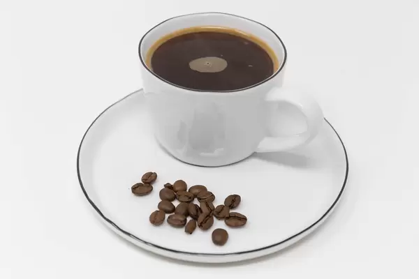 Nahaufnahme: Kaffeebohnen mit einer Tasse ganz normaler Kaffee ohne Milch vor weißem Hintergrund