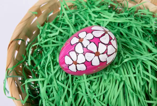 Nahaufnahme pinkes Osterei handbemalt mit weißen Blumen auf Ostergras in Bastkörbchen