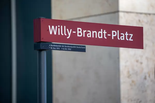 Nahaufnahme: rotes Schild "Willy-Brandt-Platz" vor dem neuen Flughafen BER in Berlin