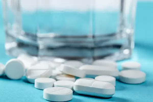 Nahaufnahme unterschiedliche Tabletten vor Wasserglas auf blauem Hintergrund