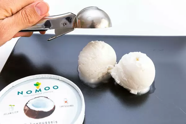 Nahaufnahme vom veganen Nomoo Kokoseis, Eislöffel in einer Hand und fertige Eiskugeln
