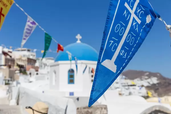 Nahaufnahme von blauer Fahne auf Santorin mit blauer Kuppel einer Kirche im Hintergrund