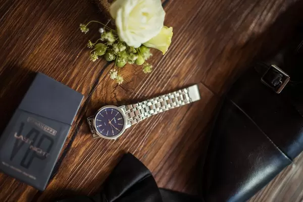 Nahaufnahme von Bräutigam-Accessoires wie Blumengesteck, Uhr und schwarze Schuhe auf Holztisch