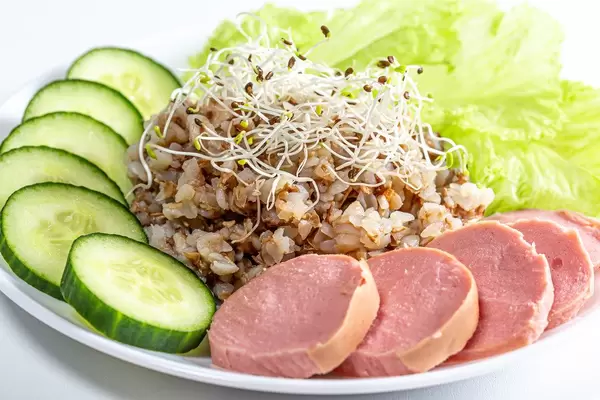 Nahaufnahme von Buchweizen mit Alfalfa-Mikrogrün, Wurstscheiben, Gurken und Salat
