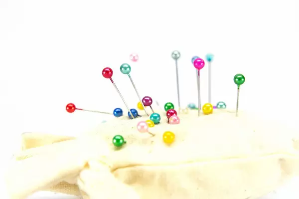 Nahaufnahme von bunten Stecknadeln in weißem Nadelkissen