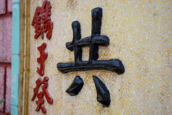 Nahaufnahme von Chinesischen Schriftzeichen in Schwarz und Rot auf dem Steintor der Phuc Kien Pagode mit Fujian-Versammlungshalle im Stadtzentrum von Hoi An, Vietnam
