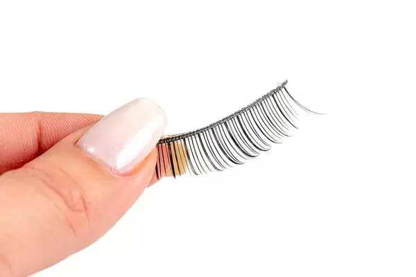 Nahaufnahme von der Hand einer Frau, die künstliche Wimpern vor weißem Hintergrund hält