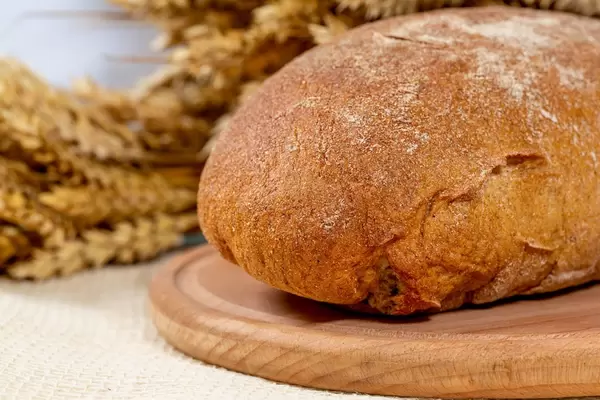 Nahaufnahme von einem Graubrot auf einem Küchenbrett mit Weizenähren