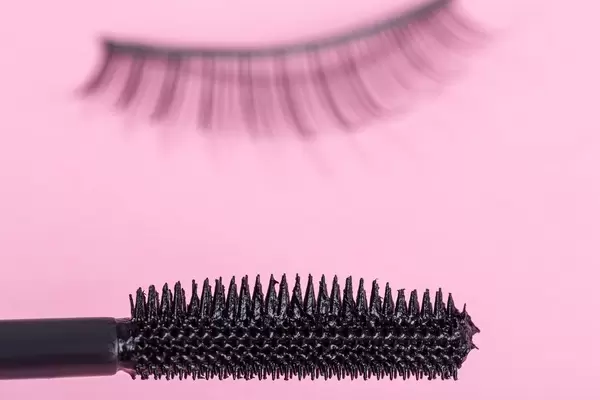 Nahaufnahme von einem Mascara-Bürsten auf pinkem Hintergrund mit künstlichen Wimpern