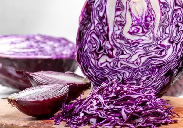 Nahaufnahme von einem Rotkohl und Zwiebeln, die geschnitten auf einem Küchenbrettchen liegen