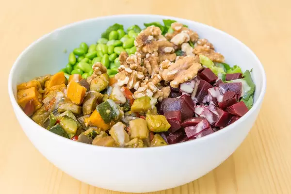 Nahaufnahme von einem veganes Bowls mit gegrilltem Gemüse, Walnüsse, Reis, Edamame und Soja-Sesam Dressing auf einem Holztisch
