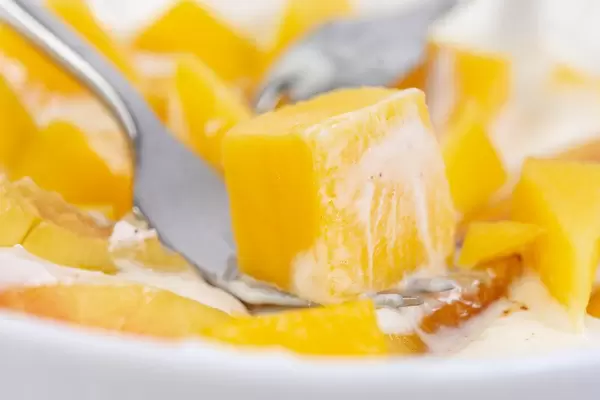 Nahaufnahme von einer Gabel mit Mangostück im griechischen Joghurt