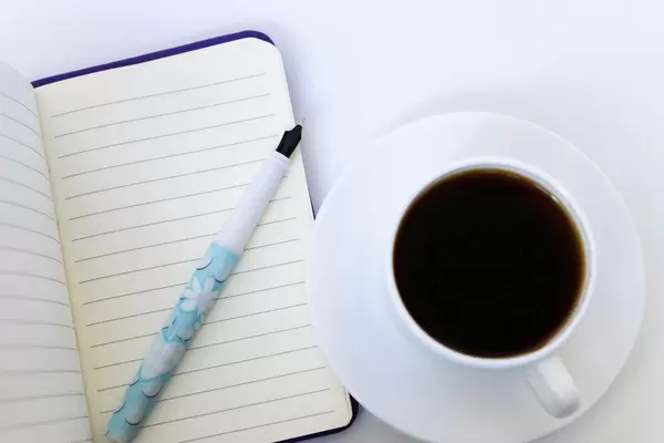 Nahaufnahme von einer Tasse Kaffee mit Notizheft und Schreibstift
