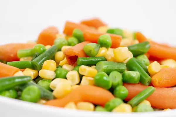 Nahaufnahme von frischen Möhren, Mais, grünen Bohnen und Erbsen in einer weißen Schüssel
