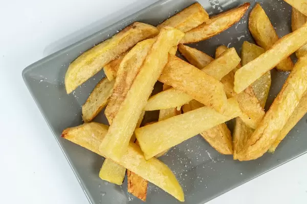 Nahaufnahme von frittierten und gesalzenen Pommes auf einem grauen Teller auf weißem Hintergrund
