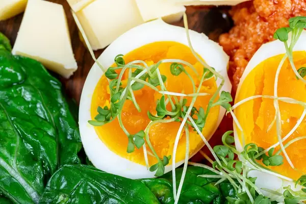 Nahaufnahme von gekochtem Ei in die Hälfte geschnitten, mit frischem Gemüse zum Frühstück serviert