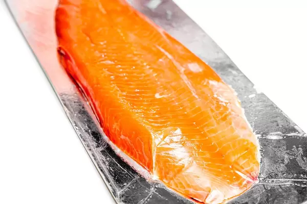 Nahaufnahme von geräuchertem roten Fischfilet, in Plastik verpackt, vor weißem Hintergrund