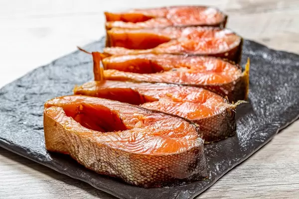 Nahaufnahme von geräucherten Lachssteaks auf schwarzem Brett in Seitenansicht