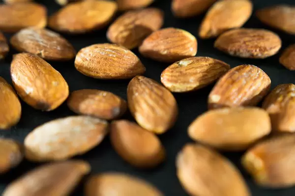Nahaufnahme von geschälten, gesalzenen Mandelkernen auf dunklem Untergrund