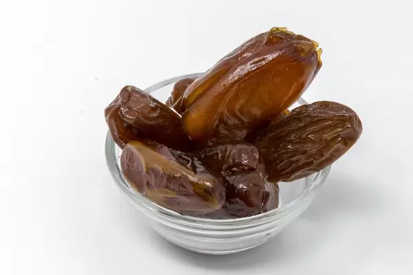 Nahaufnahme von getrockneten Datteln in Glasschälchen auf weißem Hintergrund