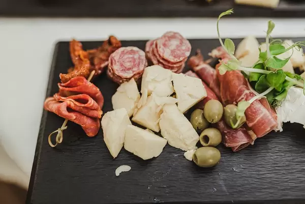 Nahaufnahme von Käsestückchen, Schinken, Oliven und Würstchen auf schwarzem Brett