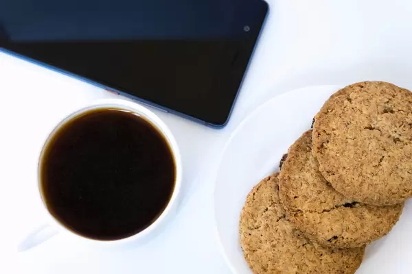 Nahaufnahme von Keksen und Kaffee mit Smartphone auf weißem Hintergrund
