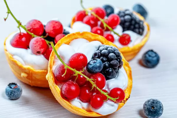 Nahaufnahme von kleinen Törtchen mit Sahne, roter Johannisbeere, Maulbeere und Heidelbeeren