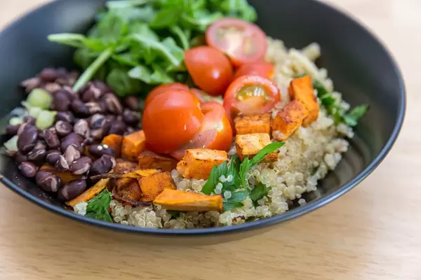 Nahaufnahme von kubanischer Quinoa-Bowl mit Süßkartoffeln, Cherry-Tomaten, Rukola und roten Bohnen