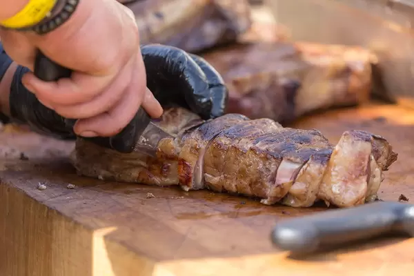 Nahaufnahme von Mann der ein großes Stück OFYR-Grillfleisch in Stücke schneidet auf Holztisch