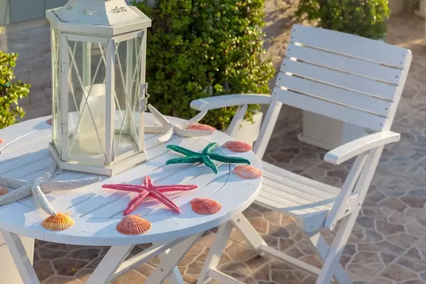 Nahaufnahme von Meeresdekoration mit Muscheln und bunten Seesternen, auf einem weißen Holztisch auf einer mediterranen Terrasse in Griechenland