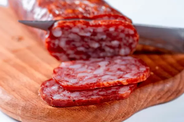 Nahaufnahme von Messer, das grobe Wurst in dünne Scheiben schneidet